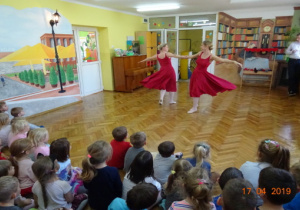 Dwie baletnice tańczą na środku sali trzymając się za ręce.